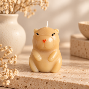 Bougie artisanale beige en forme de petit rongeur aux oreilles rondes, fond pierre beige et fleurs séchées.
