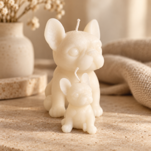 Duo de bougies sculptées ivoire représentant un bouledogue et son chiot, ambiance beige avec fleur séchée.