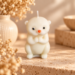 Bougie petit ourson blanc ivoire, nez orangé et mains réunies, sur travertin dans un décor naturel