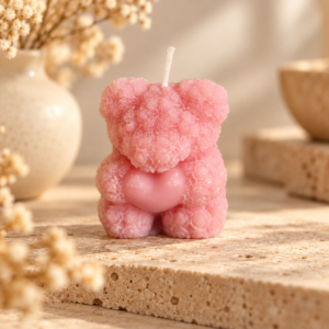 Bougie ourson rose aux reliefs floraux avec cœur rose, mise en scène naturelle sur travertin