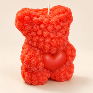 Bougie rouge en forme d'ourson recouvert de roses sculptées, tenant un cœur, sur fond crème clair.